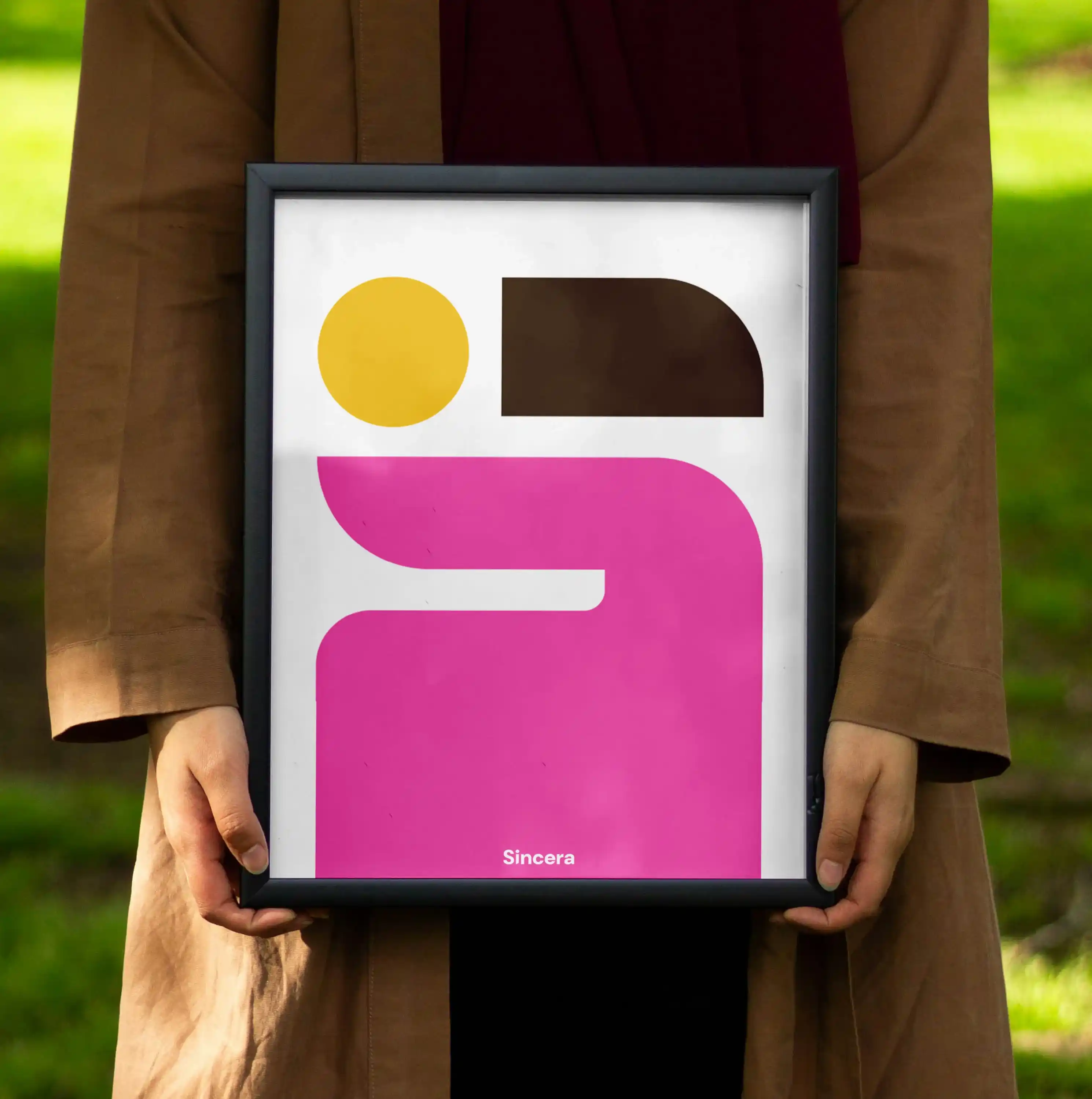 Photo d'une femme tenant une affiche dans un cadre dans un parc. L'affiche représente l'icône de Sincera communication sur fond blanc.