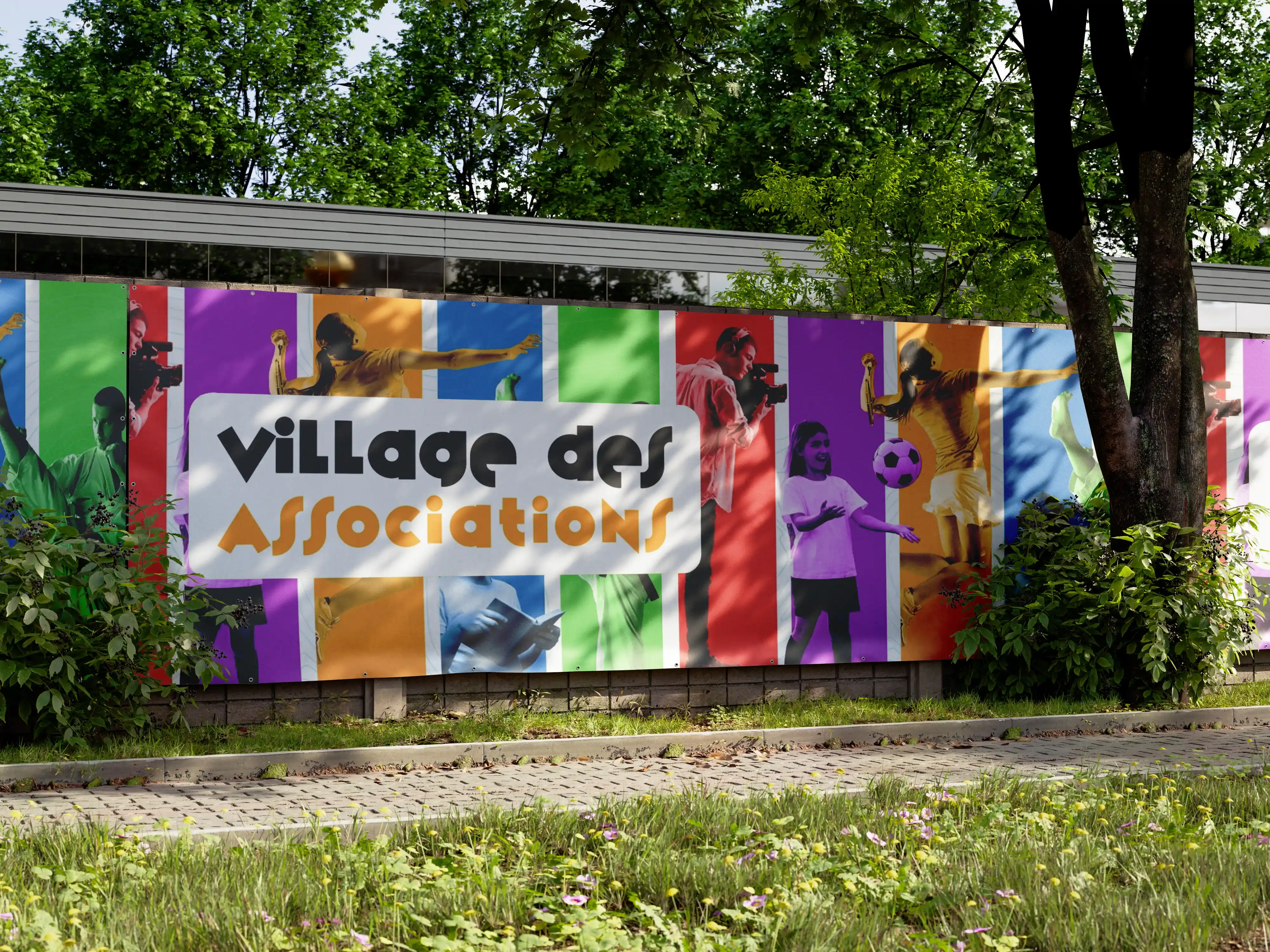 Photo d'une longue banderole dans un parc boisé. Elle est constituée du logo du village des associations avec cinq bandes colorées en dessous et des photos de sportifs ou d'artistes.